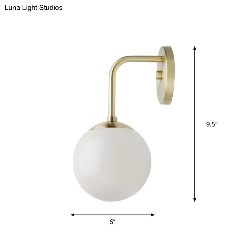 A sleek minimalist golden black wall light with a brass finish and milky glass ball shade for bedroom use