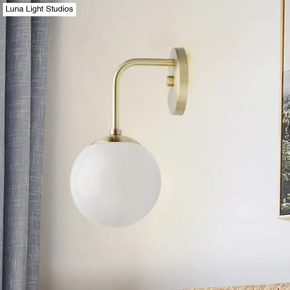 A minimalist golden black wall light with a sleek brass finish and a milky glass ball shade for bedroom use