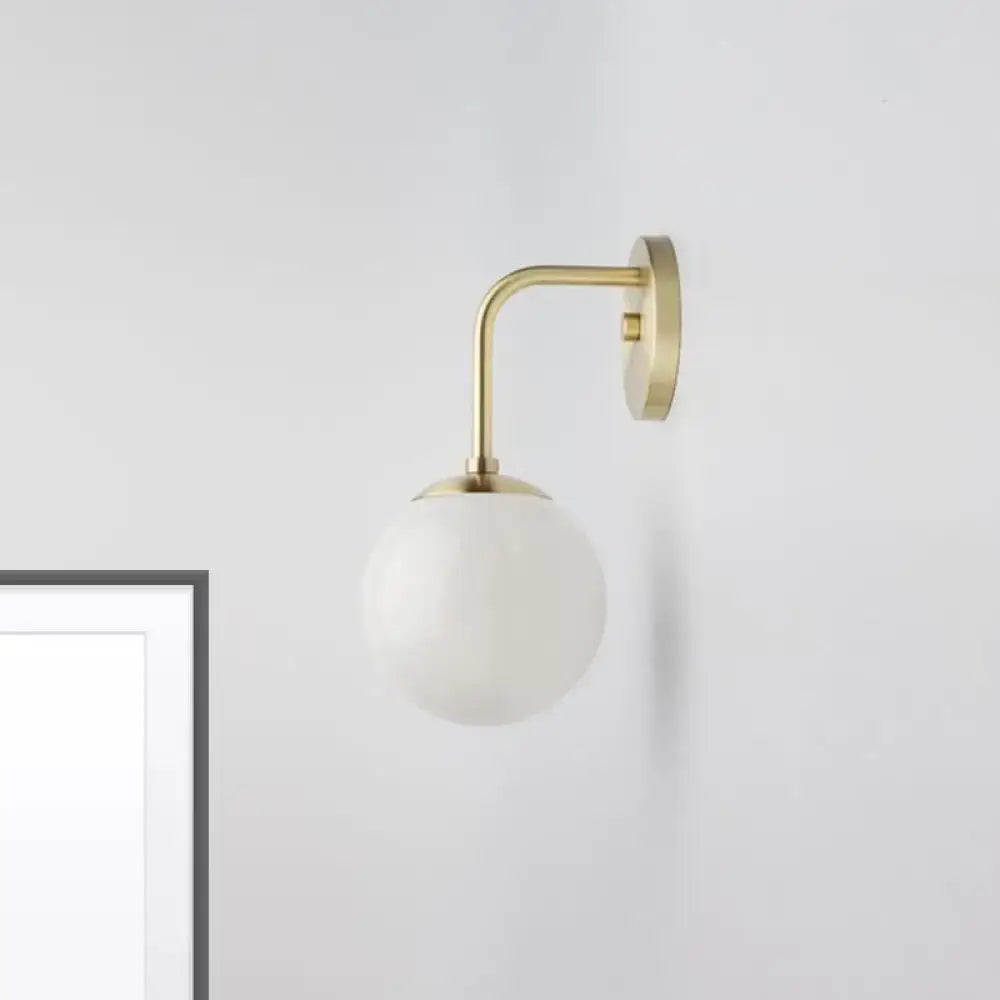A minimalist golden black wall light with brass finish and a milky glass ball shade for bedroom lighting