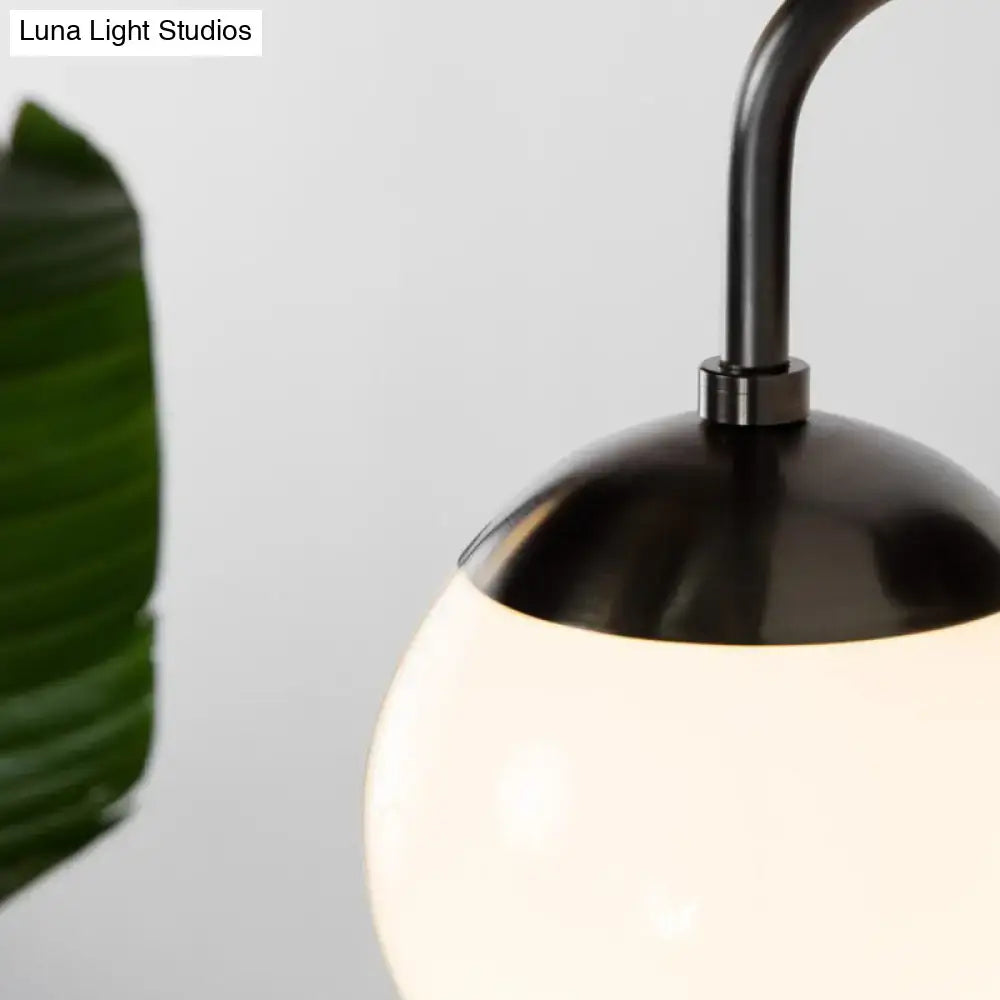 Minimalist golden black wall light features black metal arm supporting a glowing milky glass ball for bedroom use