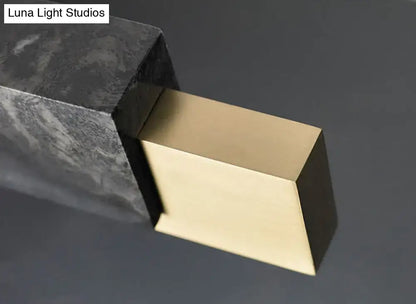 A sleek rectangular brass doorstop with polished gold metal finish complements minimalist black marble light with gold accents and black cord
