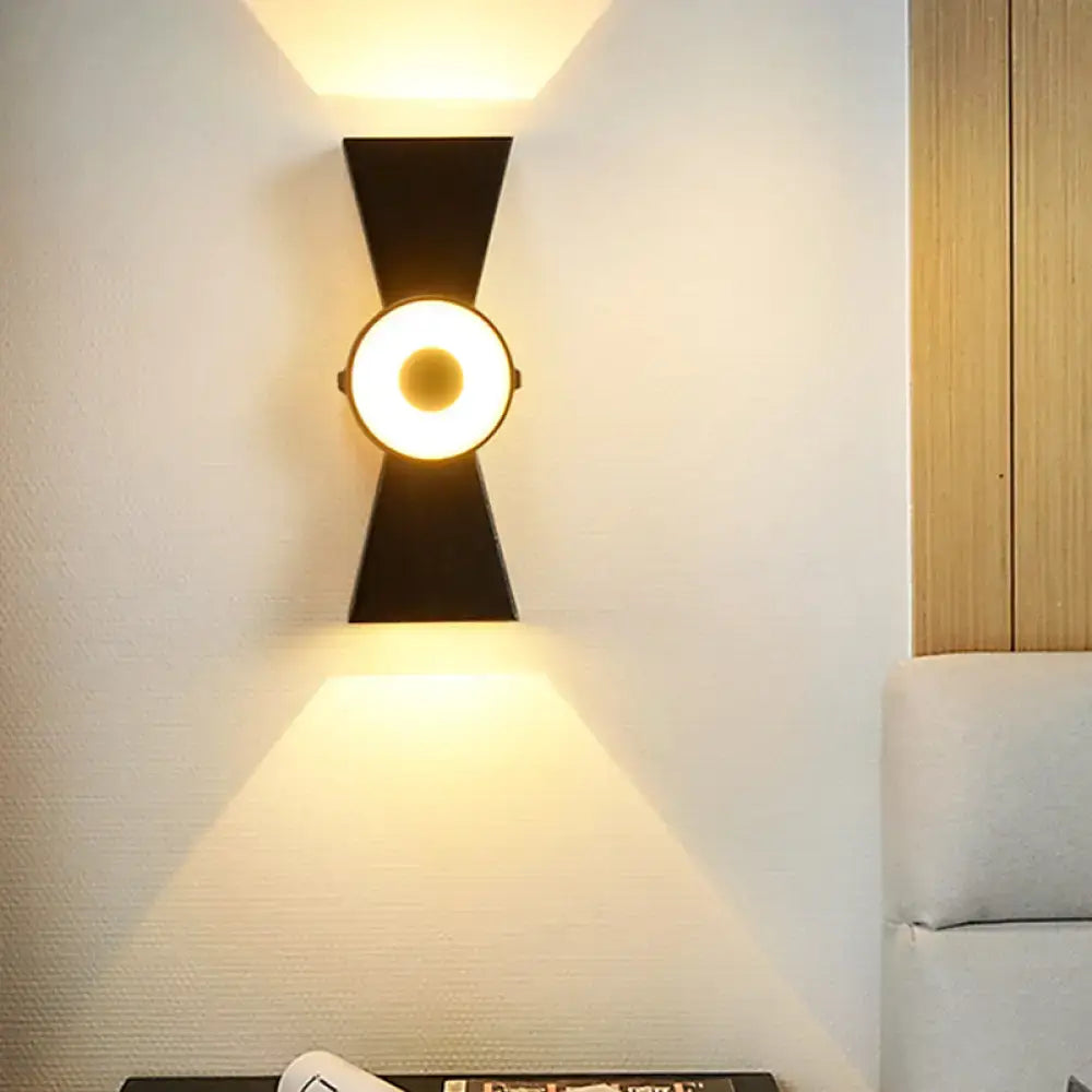 Minimalist black metal wall sconce with warm white light circular center and angular flanges for bedroom use