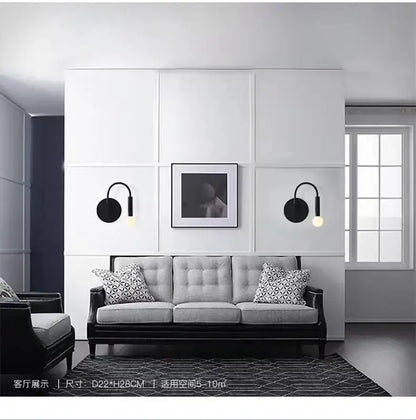 Black modern wall lamp with curved sconce and circular base featuring an exposed bulb for minimalist bedroom decorbites design