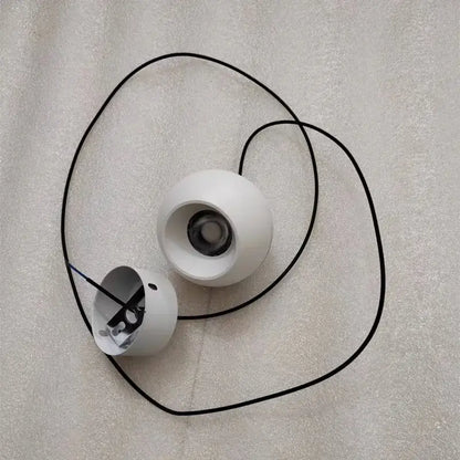 White spherical wireless speakers with black audio cables beside minimalist black and off-white die-cast aluminum pendant light with acrylic lamp holder for kitchen