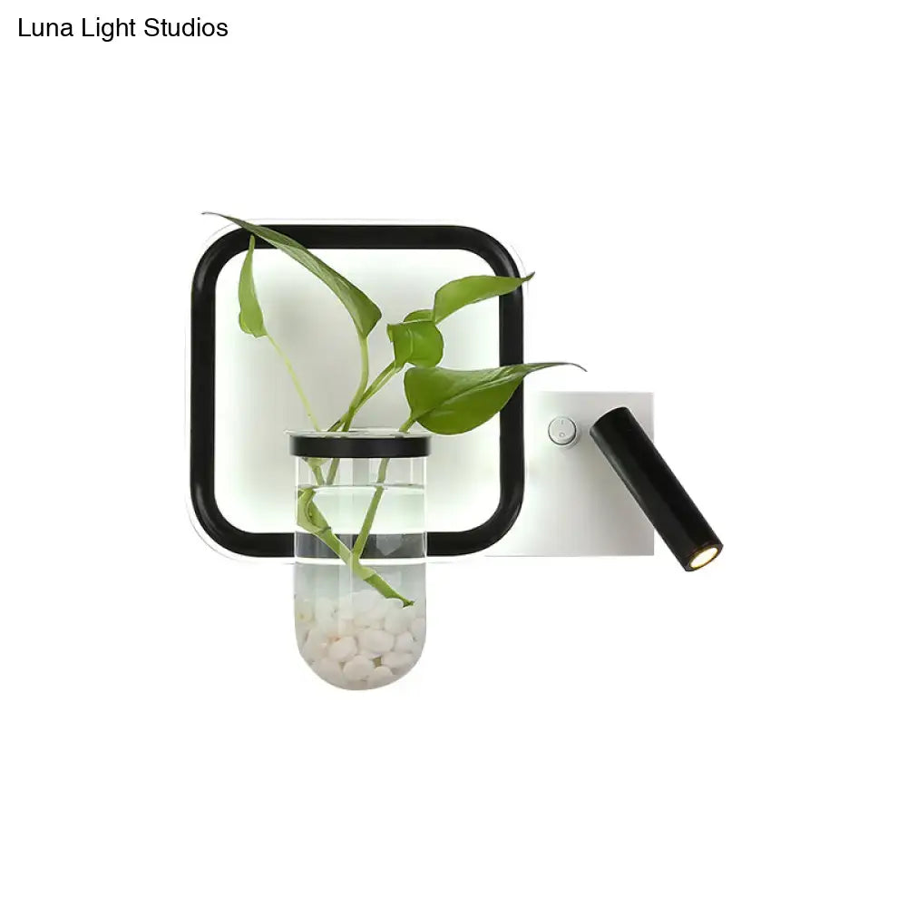 Minimalist black wall mount light with clear glass vase holding green foliage and white pebbles for bedroom sconce