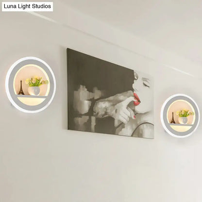 Minimalist black and white circular led wall sconce with sleek white frame soft glowing ring and inner shelf holding decor