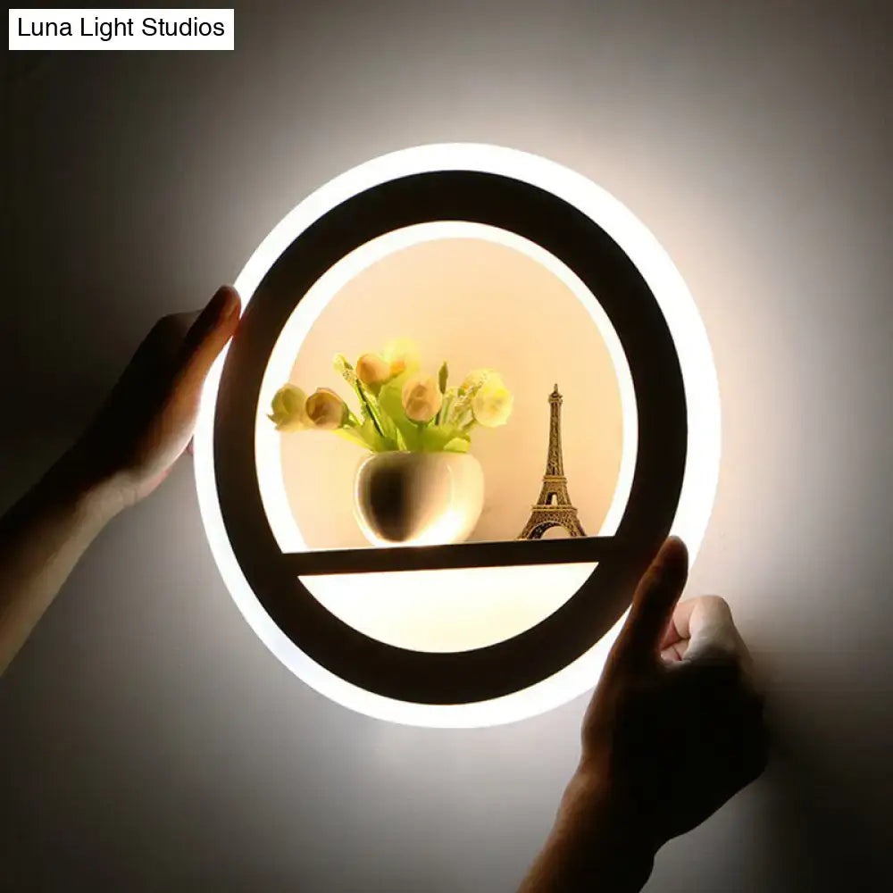 Minimalist black and white circular led wall sconce with a black frame bright white light and integrated shelf holding yellow flowers and eiffel tower model