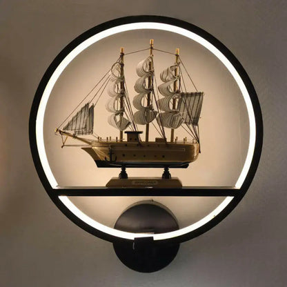 Minimalist black and white circular led wall sconce with shelf featuring a wooden three-masted sailing ship model
