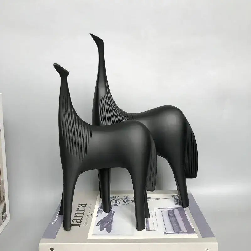 Two sleek matte black minimalist horse abstract ornaments with elongated necks and textured manes on a magazine for home decor