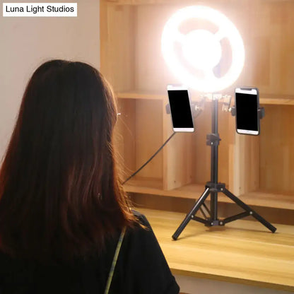 Black minimalist led ring light inch fixture with phone holder mounted on tripod holding two smartphones in bedroom setup