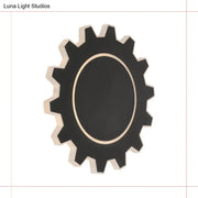 Black gear-shaped wall mirror with gold-toned inner rim complements minimalist black white led wall sconce with warm white light