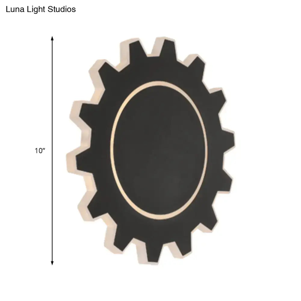 Black gear-shaped wall mirror with light-colored wooden frame and central oval surface paired with warm white light
