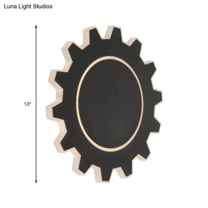 Black gear-shaped wall mirror with light-colored wooden frame and central oval surface paired with warm white light