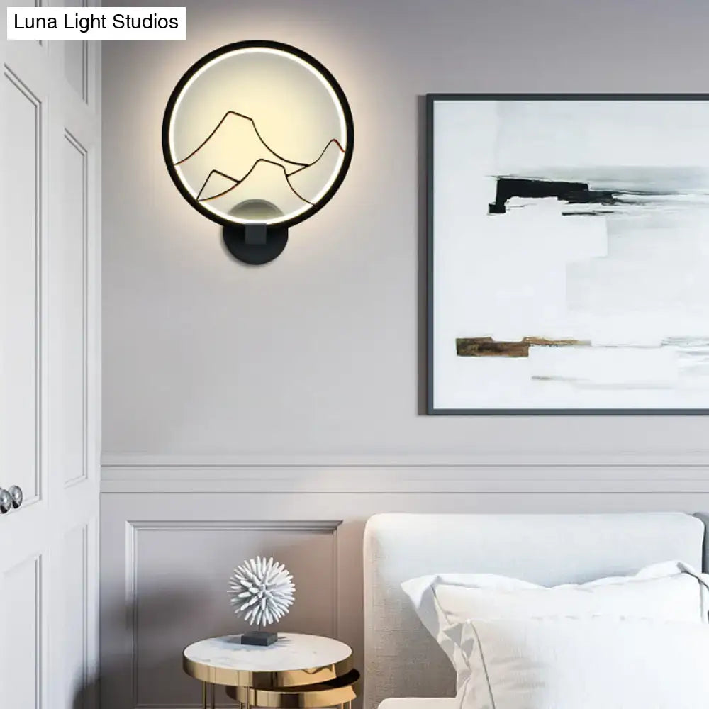 Minimalist black acrylic ring wall lamp with a glowing circular frame illuminating gold mountain silhouettes
