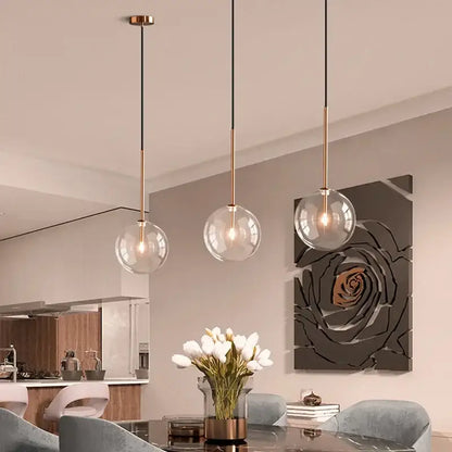 Three modern pendant lights with clear glass ball shades and brass-finished rods for dining room decorbites clear glass