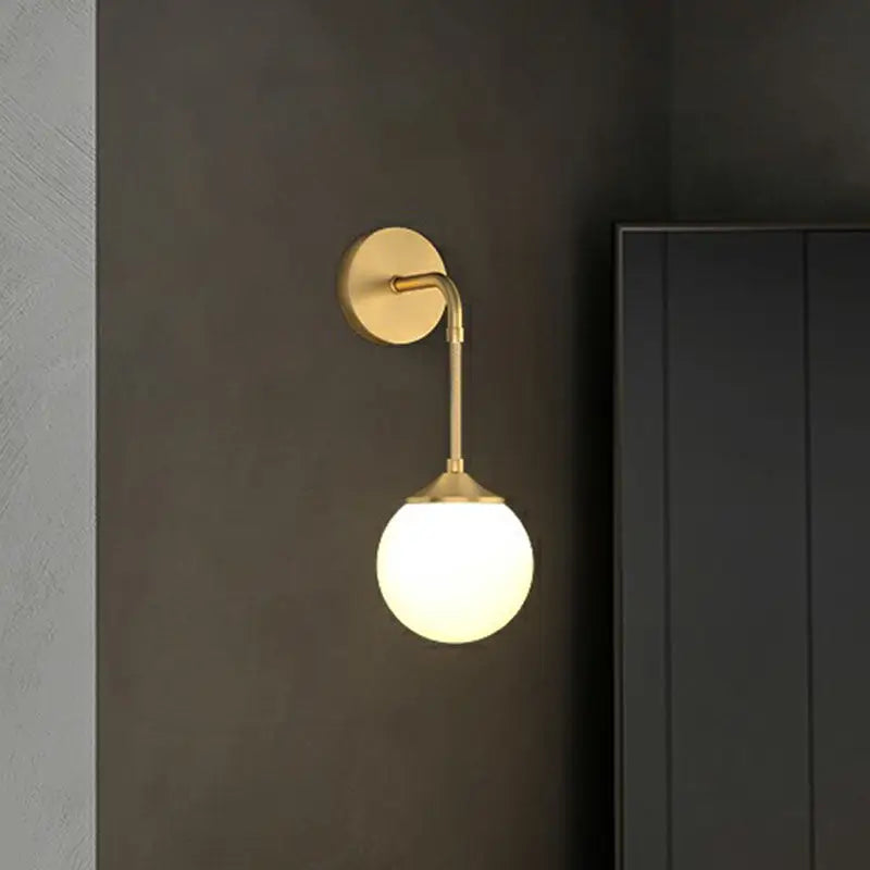 Gold-toned minimalist brass led wall lamp with spherical frosted glass globe for dining room lighting