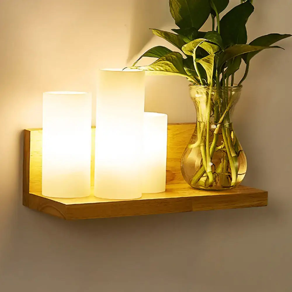 Warm-toned cylindrical led candle lights on a minimalist wooden shelf complement a brass and glass geometric wall sconce bedroom light