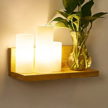 Warm-toned cylindrical led candle lights on a minimalist wooden shelf complement a brass and glass geometric wall sconce bedroom light