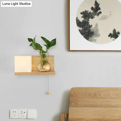 Minimalist brass and glass geometric wall sconce with wooden shelf, square glowing light panel, and glass vase with green plants