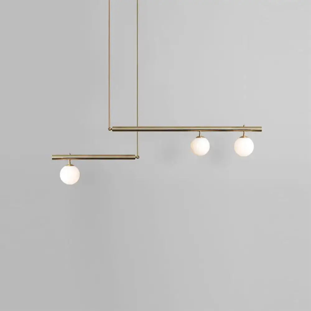 Modern minimalist brass ceiling light with three white globe glass bulbs designed for kitchen island lighting