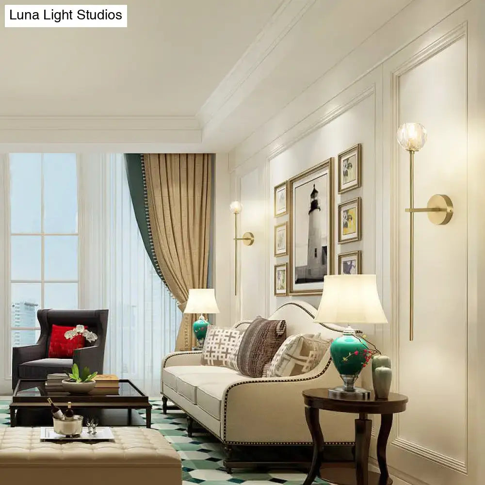 Cream-colored sofa with tufted upholstery and dark wood legs shown with a minimalist brass faceted crystal direct wired wall sconce