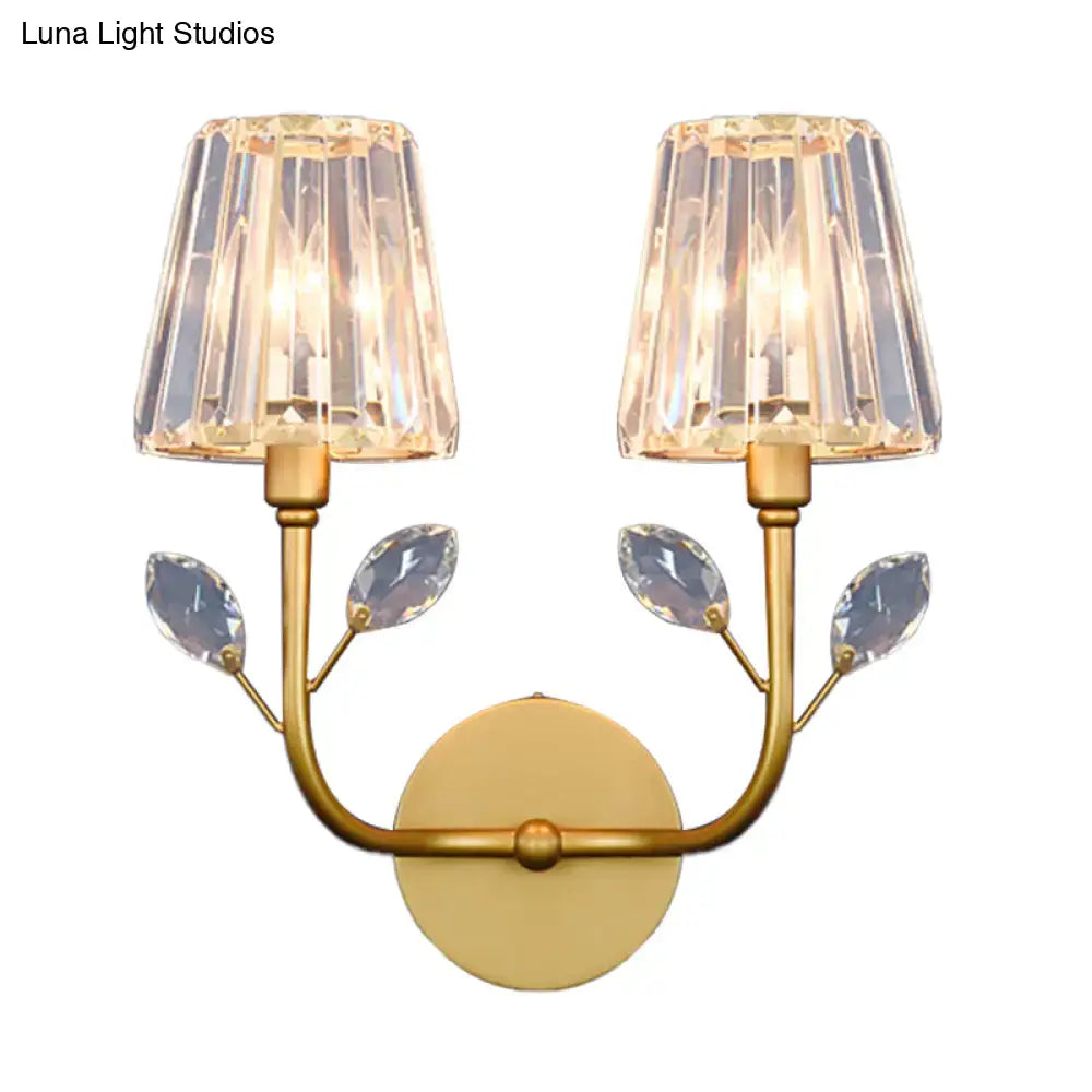 Minimalist brass finish wall sconce with gold-toned frame, two crystal lampshades, and leaf-shaped crystals wall light