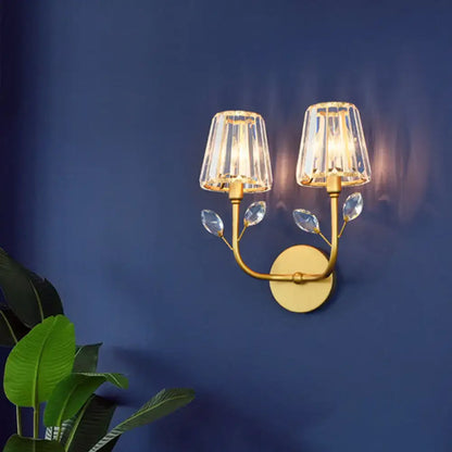 Minimalist gold-toned brass finish wall sconce with two faceted crystal shades and decorative leaf crystals wall light