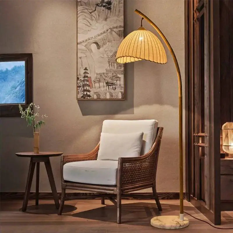 A warm-toned minimalist brass led floor lamp with a curved golden frame and woven rattan shade on marble base