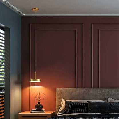 A modern brass led pendant light with a gold circular shade hangs over a wooden nightstand for minimalist decorbites pendant lights