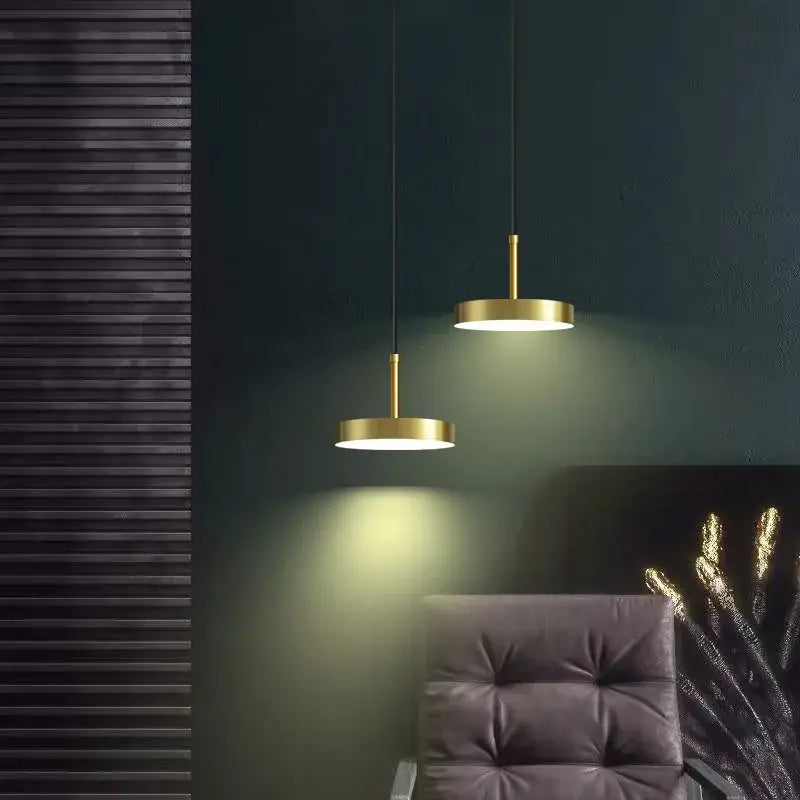 Two minimalist brass led pendant lights with circular gold shades hang from cords against a dark wall for dining room decorbites brass led pendant