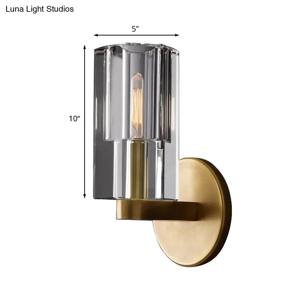Minimalist brass wall sconce with a faceted ribbed glass cylinder and exposed filament bulb base for living room lighting