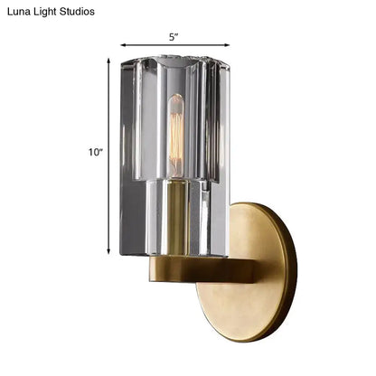 Minimalist brass wall sconce with a faceted ribbed glass cylinder and exposed filament bulb base for living room lighting