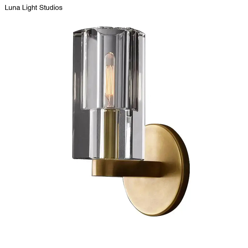Minimalist brass wall sconce with faceted clear glass cylinder and exposed filament bulb base for living room lighting