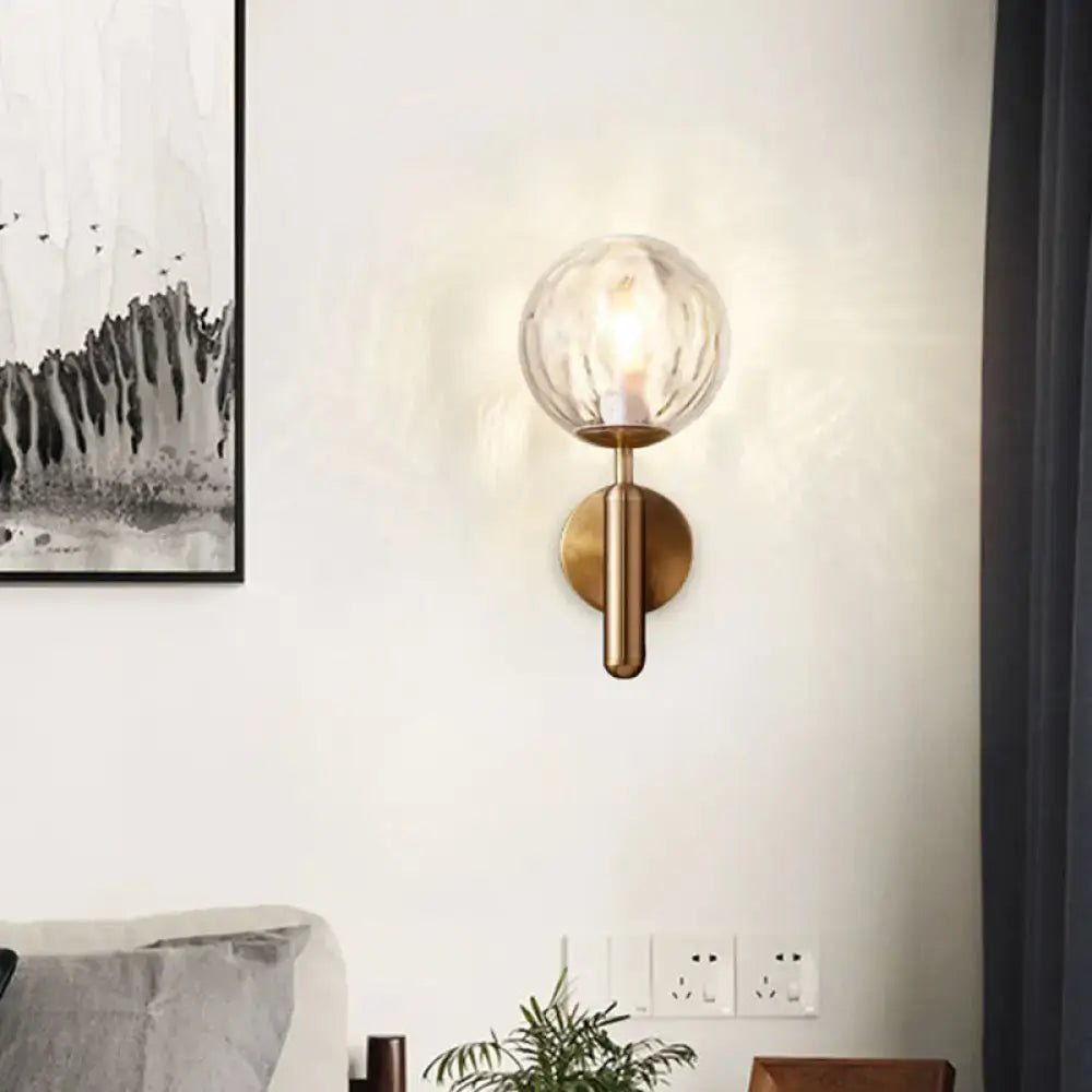 Minimalist brass wall mount light with textured spherical glass globe designed for bedroom lighting