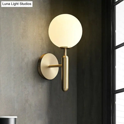 Minimalist brass wall sconce with cream glass shade for living room featuring a brass finish and frosted globe design