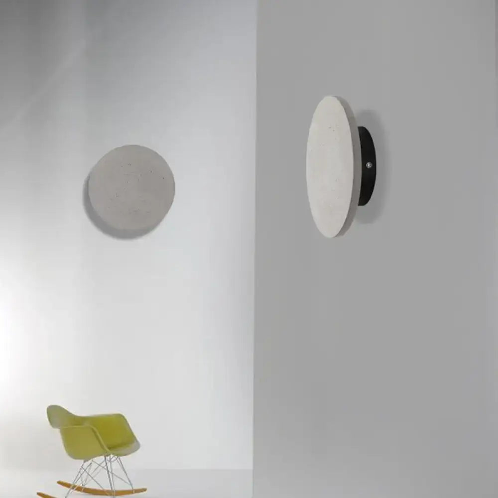 Minimalist cement grey flat round wall sconce light with a matte white disc and black mounting base for bedroom use