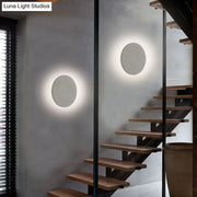 Minimalist cement grey flat round wall sconce light with matte finish emits soft ambient light for bedroom use