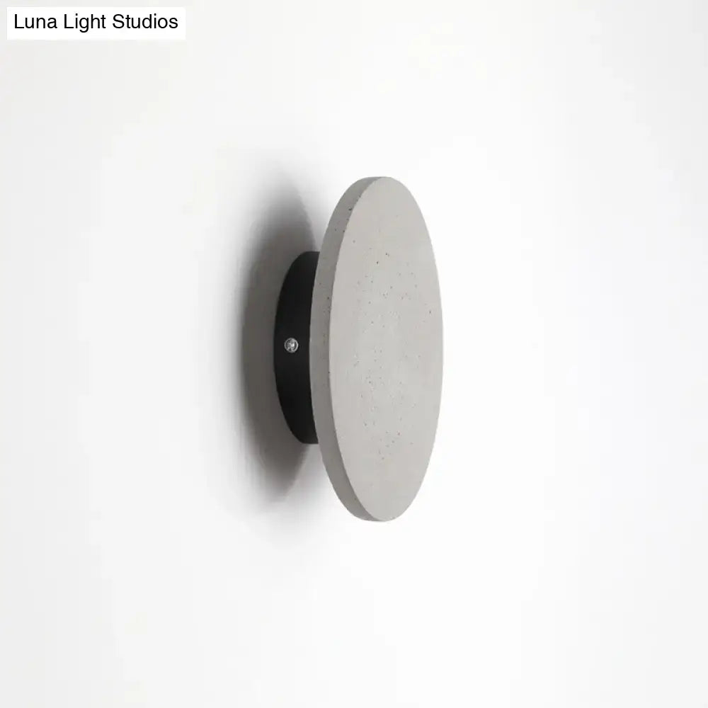 Minimalist cement grey flat round wall sconce light with a concrete disc and sleek black mounting base for bedroom use