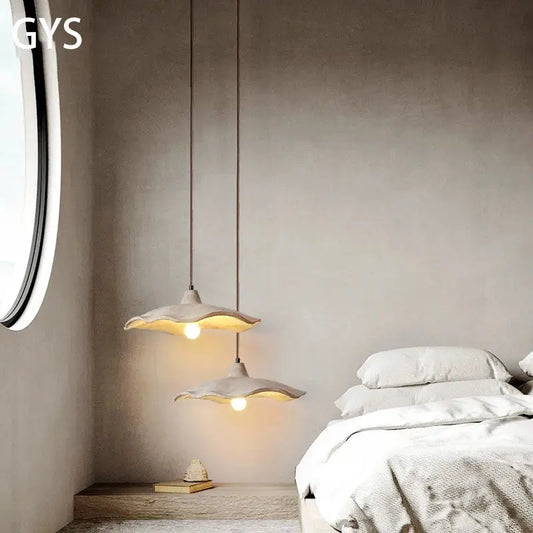 Two minimalist ceramic petal pendant chandelier lights with soft white shades hanging from cords on a concrete ceiling