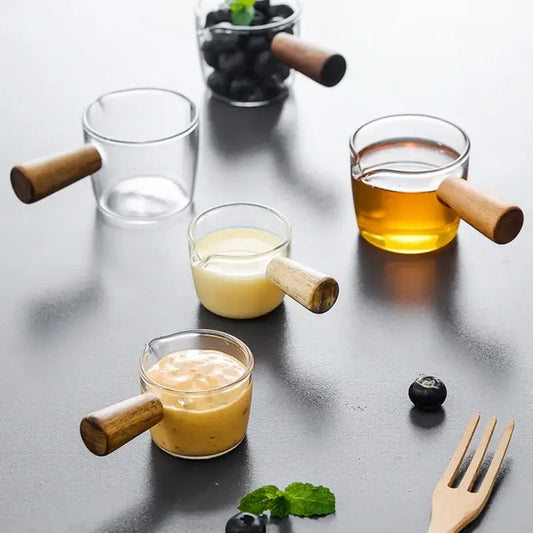 Minimalist clear glass sauce dish with wooden handle featuring multiple glass sauce cups filled with colored liquids