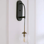 Black metal wall mounted sconce with minimalist clear glass globe and brass accents for bedroom lighting