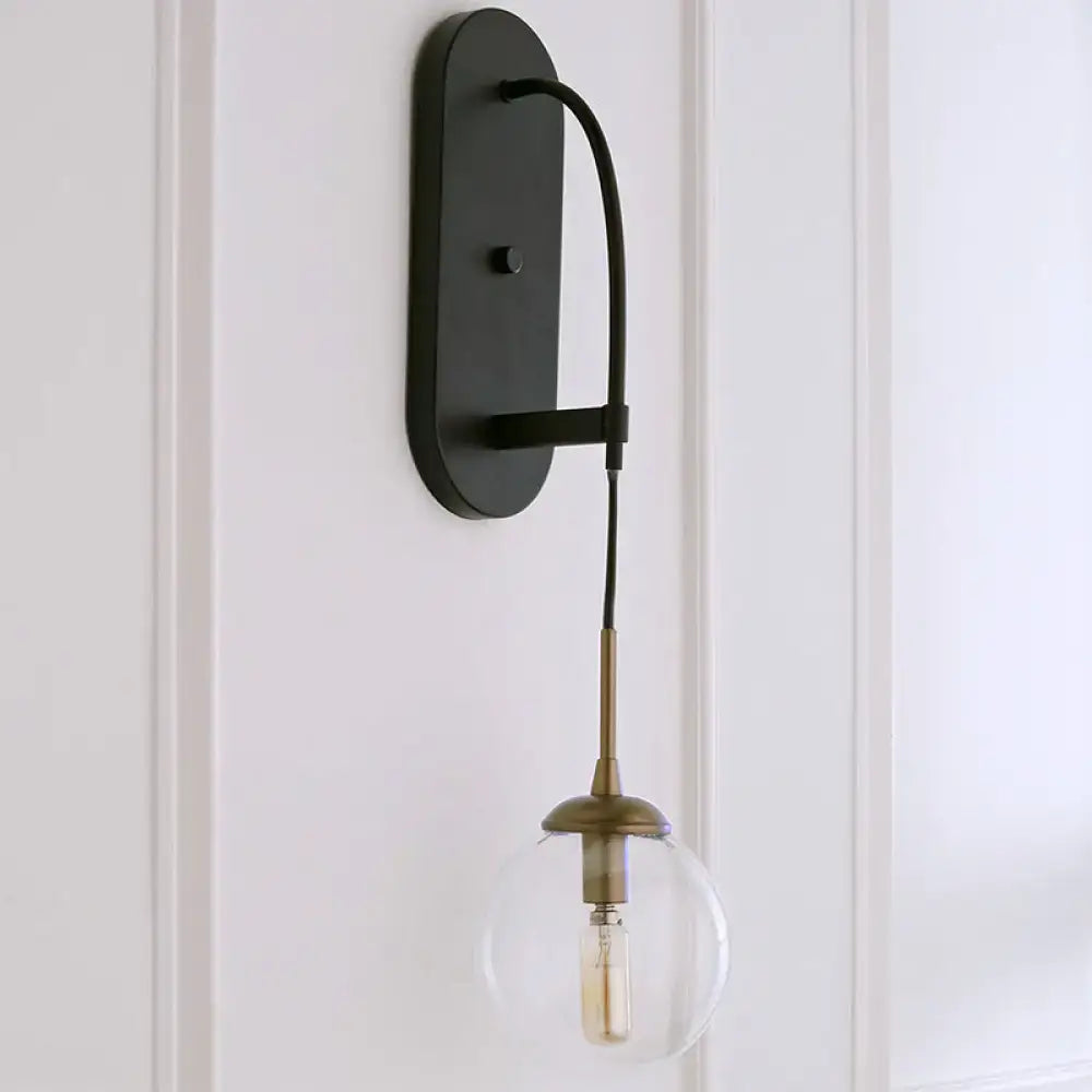 Black metal wall mounted sconce with minimalist clear glass globe and brass accents for bedroom lighting