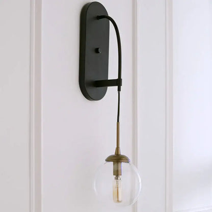 Black metal wall mounted sconce with minimalist clear glass globe and brass accents for bedroom lighting