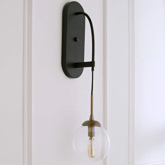 Black metal wall mounted sconce with minimalist clear glass globe and brass accents for bedroom lighting