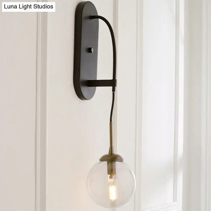 Black metal wall mounted sconce with minimalist clear glass globe and brass hardware for bedroom lighting
