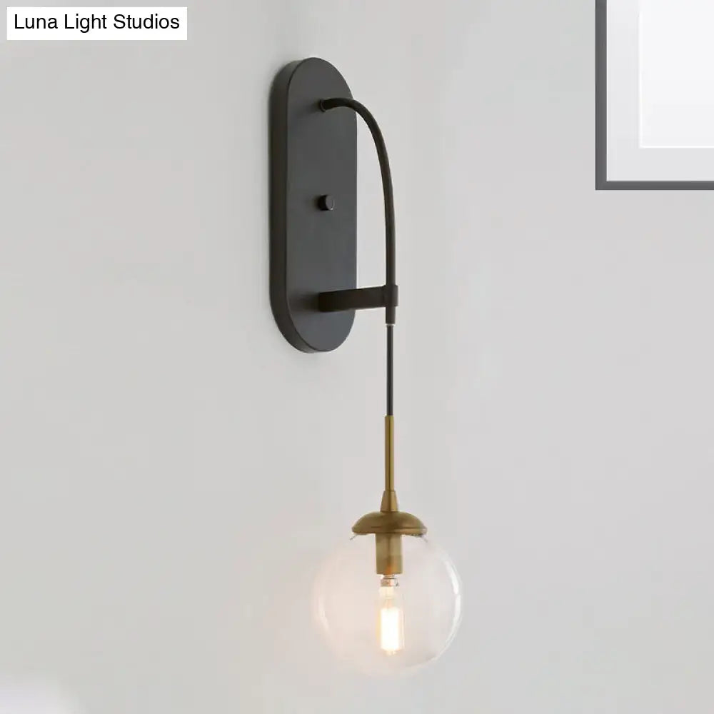 Minimalist clear glass wall mounted sconce in black and brass with a curved arm holding a clear glass globe bulb