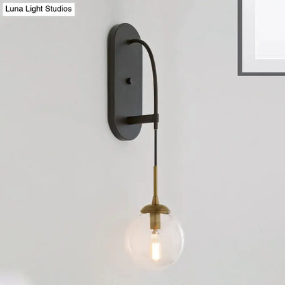 Minimalist clear glass wall mounted sconce in black and brass with a curved arm holding a clear glass globe bulb