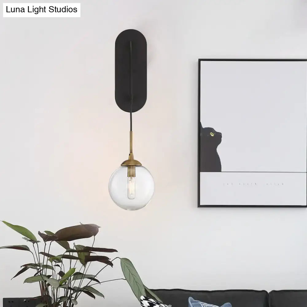 Minimalist clear glass wall mounted sconce with black and brass finish and a clear glass globe shade for bedroom lighting