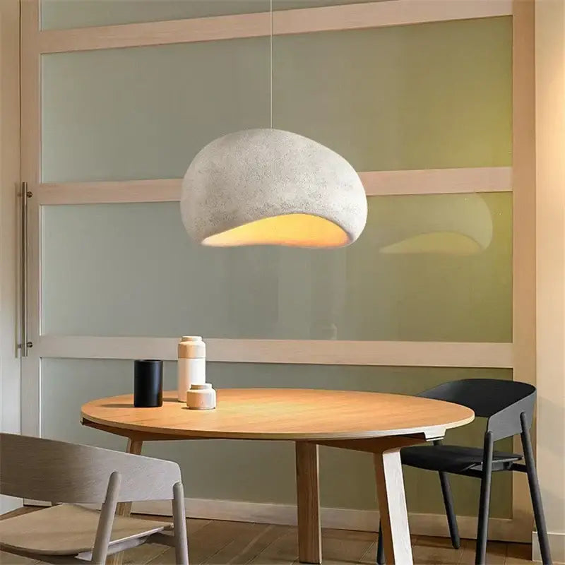 A soft white minimalist concrete decorbites cobblestone pendant light with textured rounded shape above wooden table