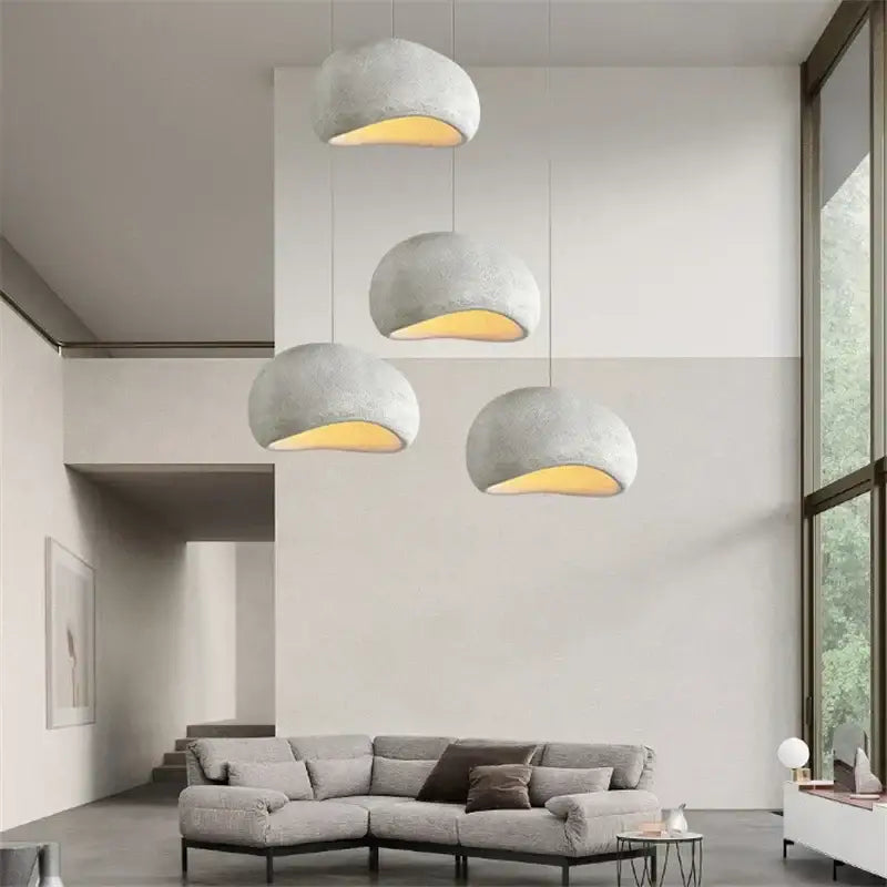 Four minimalist concrete cobblestone pendant lights with matte gray finish and warm yellow glow for dining room decor